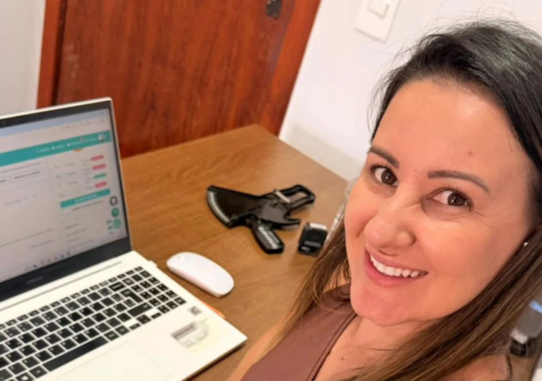 Alessandra Rodrigues sorrindo diante do notebook, na mesa do consultório